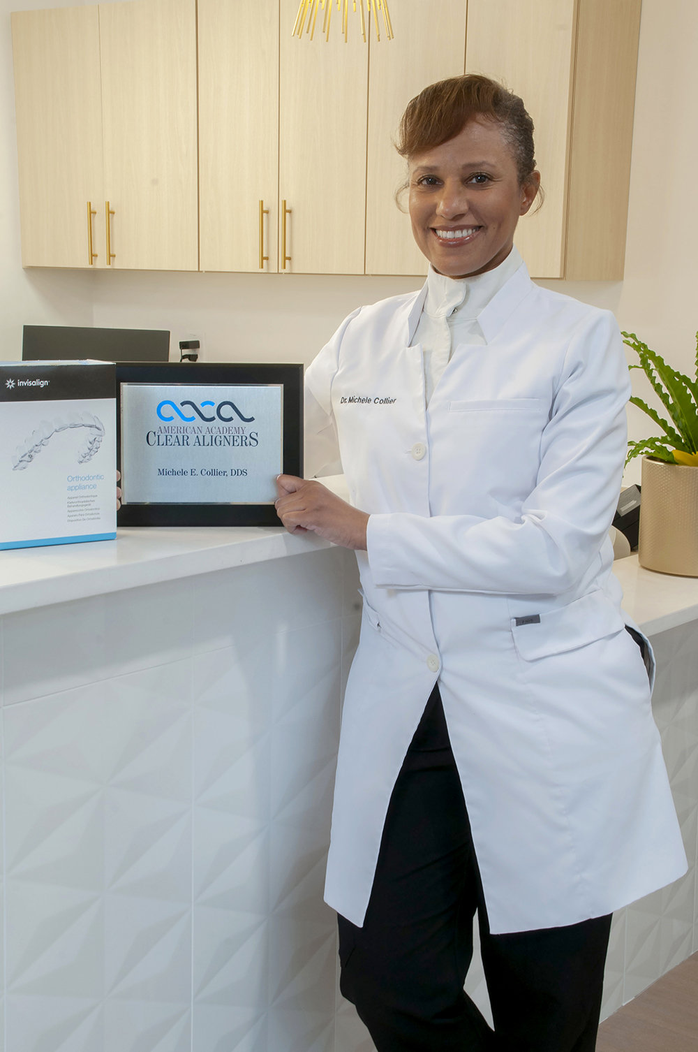 Dr. Michele Collier holding an Invisalign orthodontic appliance box and American Academy of Clear Aligners certificate